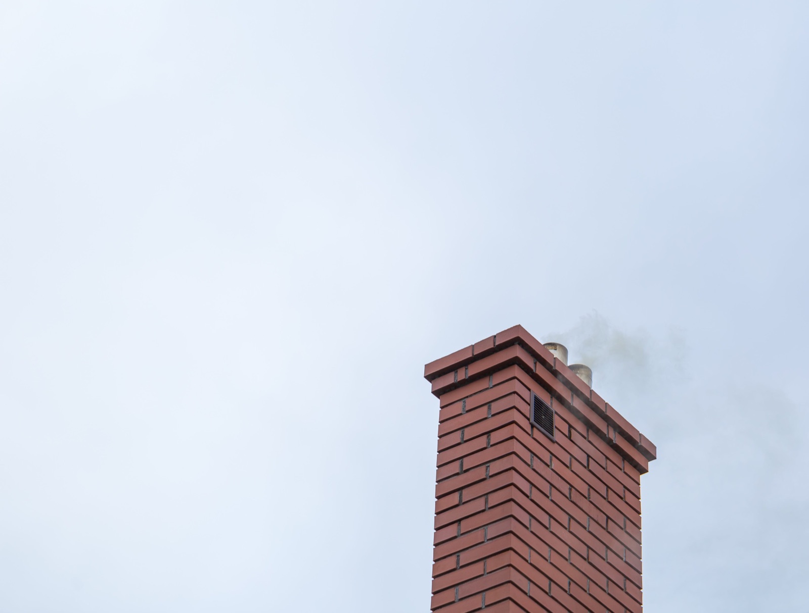Smoke rising from the top of a brick chimney